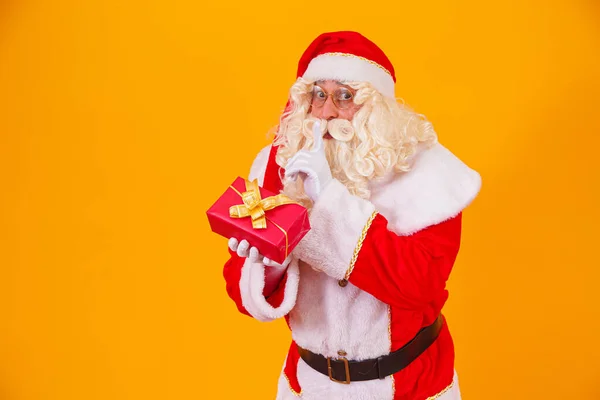 Święty Mikołaj Żółtym Tle Trzymając Prezent Rękach Czyniąc Znak Milczenia — Zdjęcie stockowe