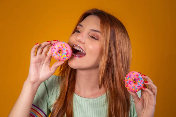 红头发的黄种女孩吃着美味的彩色甜甜圈 — 图库照片