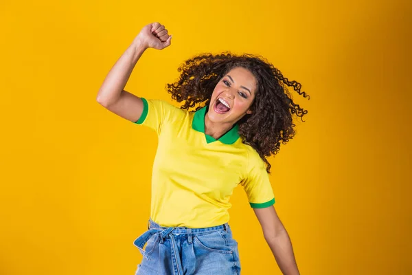 ブラジルのファン 黄色の背景でサッカーやサッカーの試合を祝うブラジルのファンを祝うためにジャンプします ブラジルの色 — ストック写真