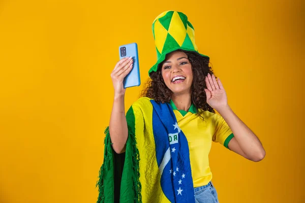 ブラジルのサポーター サッカーを祝うブラジルの女性ファン 黄色の背景にサッカーの試合 ブラジル色 セルフィースマートフォン — ストック写真