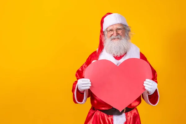 サンタクロースは黄色の背景に大きな赤いハートカードを持っています ロマンチックなサンタクロース — ストック写真