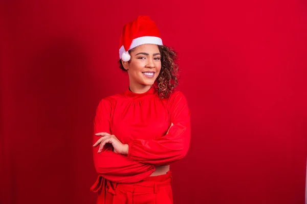 赤い背景に腕を組んでクリスマスの帽子をかぶったアフロの女性 孤立した肖像 — ストック写真