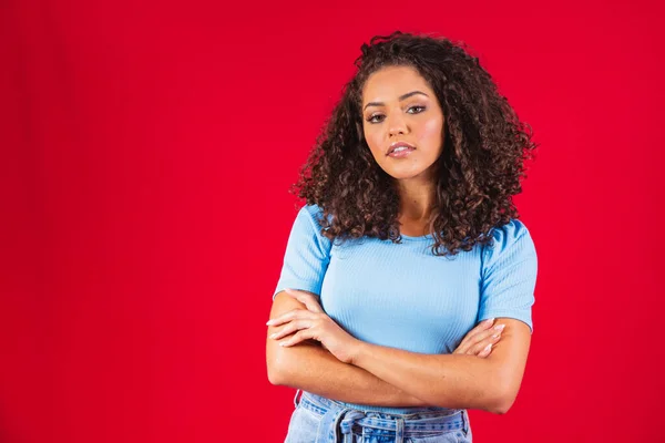 stock image Beauty portrait of a Brazilian woman with afro hairstyle and glamour makeup. Latin woman. Mixed race. Curly hair. Hair style. Red background. Cross arms