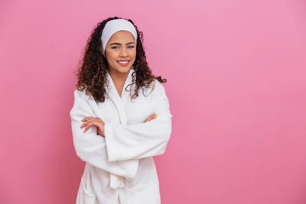白いバスローブを着た美しいアフロの女の子テキストのためのスペースとピンクの背景にサッシ 健康とケアの概念です クロスアーム — ストック写真
