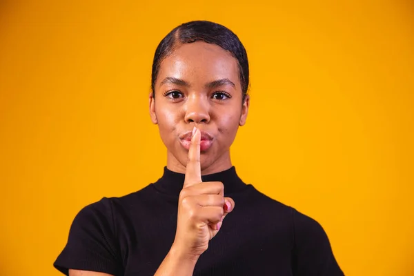 Secret, gossip concept. Young woman whispering a secret behind her hand. Business woman isolated on trendy yellow studio background. Young emotional afro woman. Human emotions, facial expression