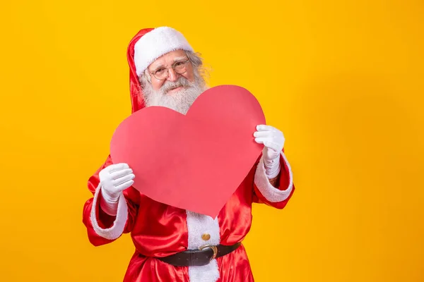 Der Weihnachtsmann Hält Eine Große Rote Herzkarte Vor Gelbem Hintergrund — Stockfoto