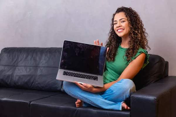 年轻女子坐在沙发上 手里拿着带有空白屏幕的笔记本电脑 上面有文字空间 — 图库照片
