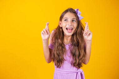 Çocukluk hayalleri ve umutları. Gözleri kapalı, şans dileyen, mucizeyi bekleyen sevimli küçük bir kızın portresi. Sarı arka planda izole edilmiş kapalı stüdyo çekimi.