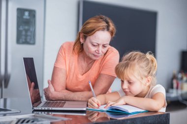 Gülümseyen olgun bir anne, kızına ev işleri hazırlamada yardımcı olur. Çevrimiçi eğitim kavramı.
