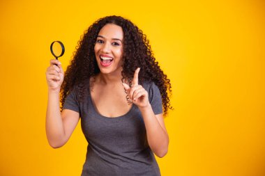 Genç, mutlu, koyu tenli bir kadının fotoğrafı el ele tutuşup cam mercekleri büyütüyor. Sarı arka planda iyi bir ruh hali var.