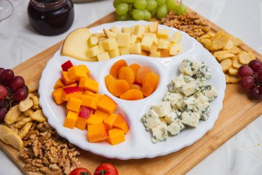 Masada çeşit çeşit aperatiflerle peynir tabağı. Masada çilek, kayısı, üzüm ve tahıllı peynir tabakları var.