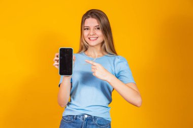 Genç sarışın kız boş akıllı telefon ekranı gösteriyor ve kameraya bakıp gülümsüyor..