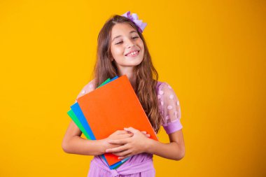 Okula giderken elinde kitaplarla gülümseyen güzel bir kız. yakın plan, izole edilmiş sarı arka plan, çocukluk. Çocuk kucaklama defterleri. Yaşam tarzı, ilgi, hobi, boş zaman, boş zaman