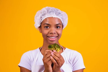 Brokoli yiyen mutlu bir afro kadın. Sarı arka planda brokolisi olan kadın. sağlıklı yeme kavramı