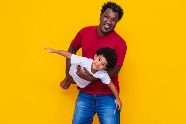 Baba ve afro oğul sarı arka planda gülümsüyor ve oynuyorlar. Babalar Günü Konsepti