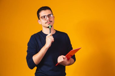 Sarı arka planda düşünen ve defterini tutan öğrenci portresi..