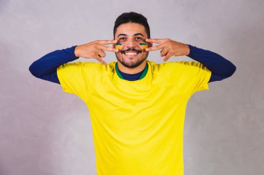 Brezilyalı bir hayran. Brezilya taraftarı, boyanın makyaj malzemesi olarak gri arka planda futbol ya da futbol maçını kutluyor. Brezilya 'nın Renkleri.