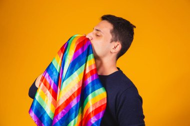 Gay gururu. Sarı arka planda lgbt bayrağını öpen homoseksüel çocuk.