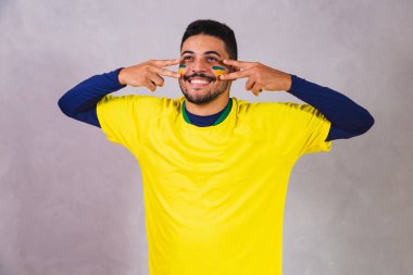 Brezilyalı bir hayran. Brezilya taraftarı, boyanın makyaj malzemesi olarak gri arka planda futbol ya da futbol maçını kutluyor. Brezilya 'nın Renkleri.