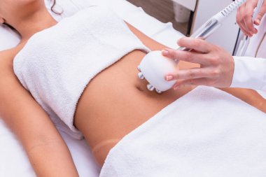 Profesyonel bir dermatoloğun bir kadının midesine radyoaktivite kaldırma prosedürü uyguladığı görüntüler. Kozmetoloji kliniğinde karın üstü tedavi gören bir kadın hasta.