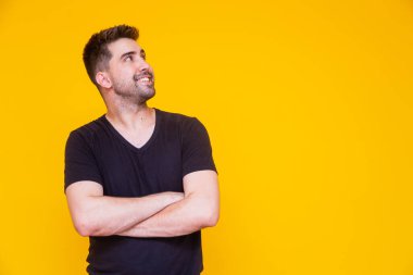 Sarı arka planda kollarını kavuşturmuş genç yakışıklı çocuk mesaj atmak için boş yere bakıyor..