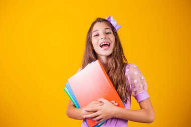 Okula giderken elinde kitaplarla gülümseyen güzel bir kız. yakın plan, izole edilmiş sarı arka plan, çocukluk. Çocuk kucaklama defterleri. Yaşam tarzı, ilgi, hobi, boş zaman, boş zaman