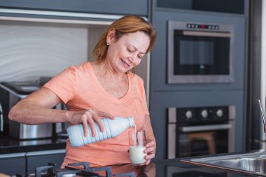 İçki içmek için bardağına bir şişe süt yapıştıran yaşlı bir kadın..