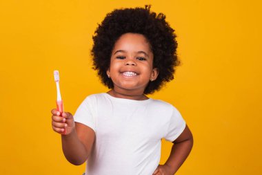 Dişlerini fırçalayan küçük tatlı bir Afrikalı Amerikalı kız, sarı arka planda izole edilmiş. Sağlıklı diş konsepti.