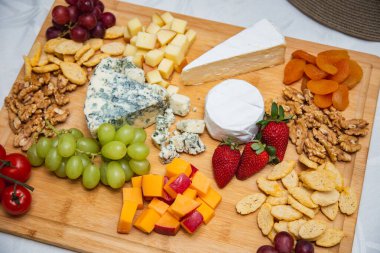 Masada çeşit çeşit aperatiflerle peynir tabağı. Masada çilek, kayısı, üzüm ve tahıllı peynir tabakları var.