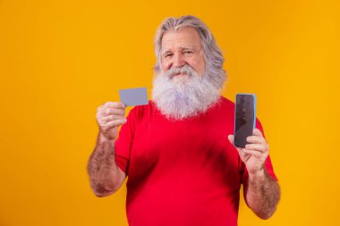 Elinde kredi kartı ve elinde boş ekranla elinde akıllı telefon tutan yakışıklı bir Noel Baba portresi..