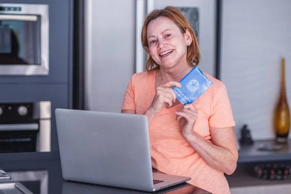 Elderly woman holding Brazilian work card and computer. Elderly woman holding workbook with home office concept.