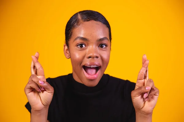 stock image Young beautiful afro woman, stylish, gesturing with her finger crossed, smiling with hope and eyes closed. Luck and superstitious concept.