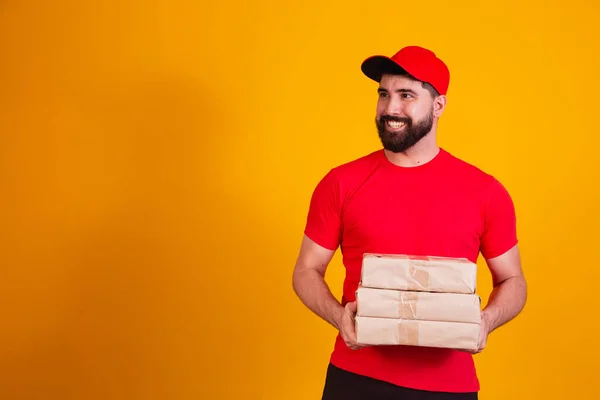 stock image Best Service Concept. Smiling caucasian delivery man in red cap and stacking holding stack of cardboard boxes while standing isolated over yellow studio background. Mail carrying packages