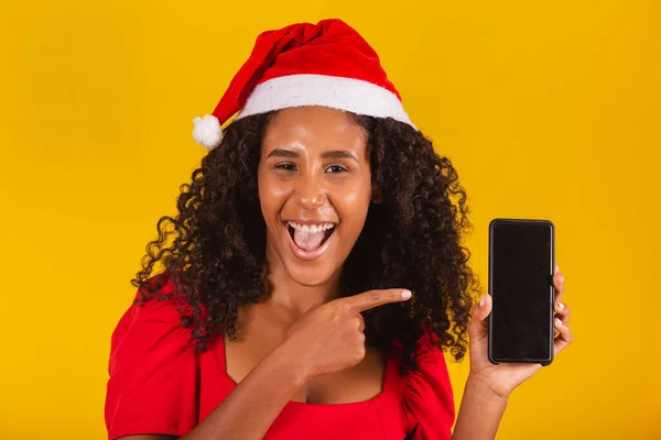 戴着圣诞礼帽的年轻圣诞老人女人微笑着 手里拿着手机 空白屏幕与黄色背景隔离 — 图库照片