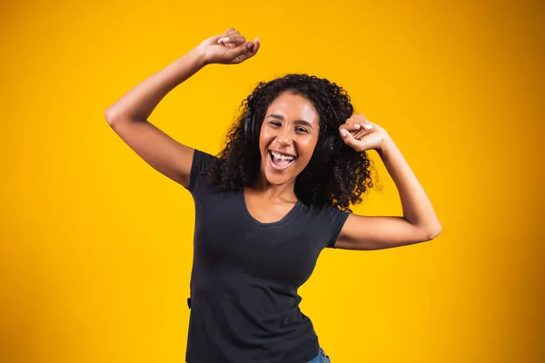 年轻的非洲女人 戴着耳机 孤零零地在黄色的墙上跳舞 听着音乐开开开心心地笑着 — 图库照片