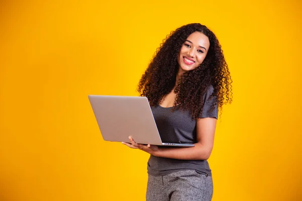 Remote work! Portrait of excited young afro woman holding laptop computer isolated over yellow background. Copyspace for text.