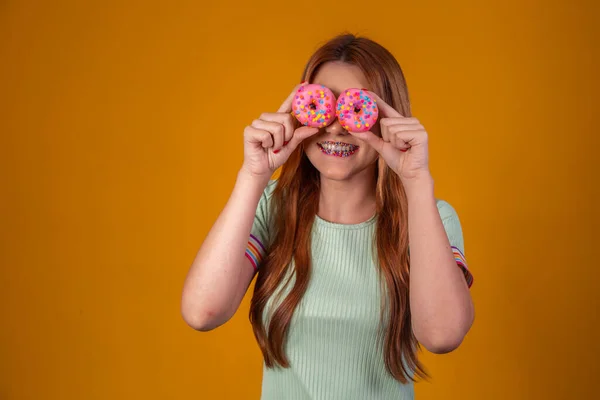 一头长发的时髦女孩摆出积极的姿势 手里拿着新鲜的粉红甜甜圈 随时可以享用甜食 — 图库照片