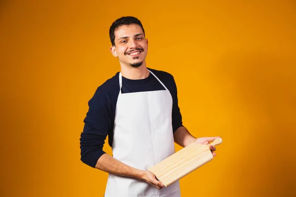 man in white apron holding a chopping board.