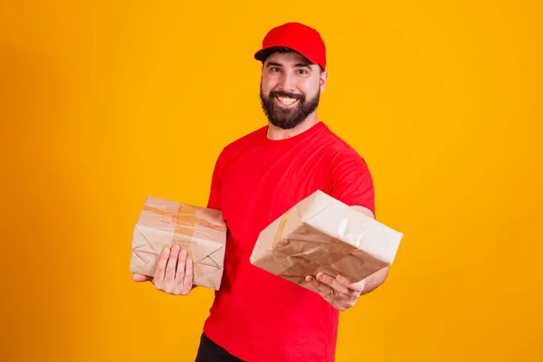 最佳服务概念 面带微笑的高加索送货员在红色的帽子和堆栈纸板箱 同时站在黄色的工作室背景孤立 携带包裹的邮件 — 图库照片