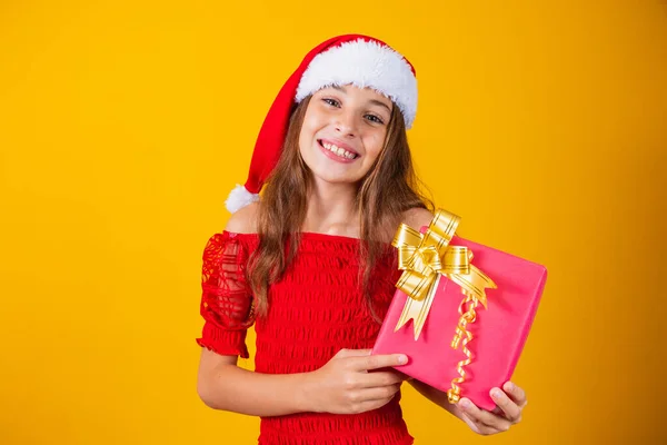 stock image cute cheerful girl in a Christmas hat on a colored background holding a gift