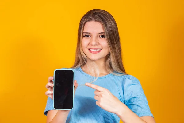Young Blonde Girl Showing Blank Smartphone Screen Pointing While Looking — Stock Photo, Image