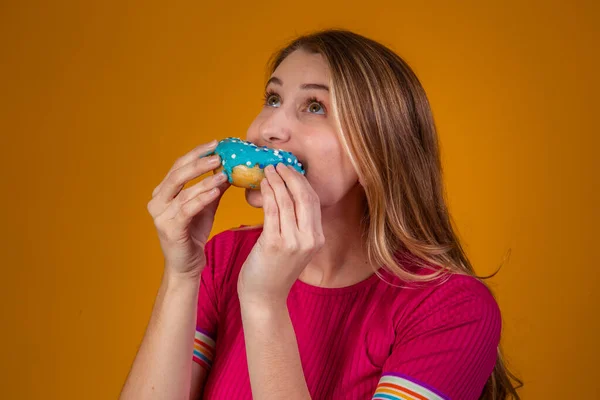 一个年轻的金发女孩吃着美味的彩色甜甜圈的画像 — 图库照片