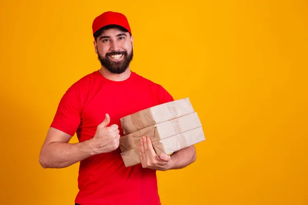 最佳服务概念 面带微笑的高加索送货员在红色的帽子和堆栈纸板箱 同时站在黄色的工作室背景孤立 携带包裹的邮件 — 图库照片