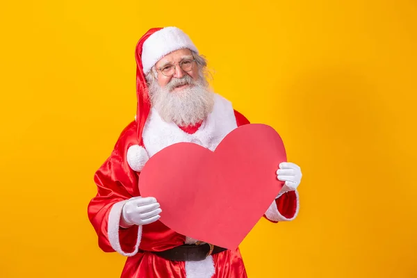 Der Weihnachtsmann Hält Eine Große Rote Herzkarte Vor Gelbem Hintergrund — Stockfoto
