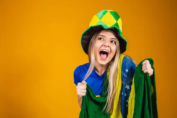 金发碧眼的巴西粉丝在黄色的背景上举着巴西国旗庆祝 — 图库照片