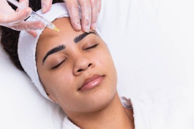 Estetik ameliyat. Genç Afrikalı kadın güzellik kliniğinde kaş bölgesinde botoks yaptırıyor. Yakın plan, fotokopi odası. Genç Afrikalı kadın alnına botoks yaptırıyor..