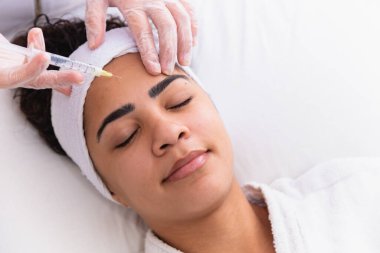 Estetik ameliyat. Genç Afrikalı kadın güzellik kliniğinde kaş bölgesinde botoks yaptırıyor. Yakın plan, fotokopi odası. Genç Afrikalı kadın alnına botoks yaptırıyor..