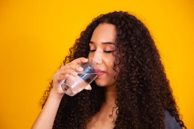 Sarı arka planda su içen güzel afro kadın. Mesaj için yer var..