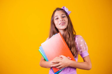 Okula giderken elinde kitaplarla gülümseyen güzel bir kız. yakın plan, izole edilmiş sarı arka plan, çocukluk. Çocuk kucaklama defterleri. Yaşam tarzı, ilgi, hobi, boş zaman, boş zaman
