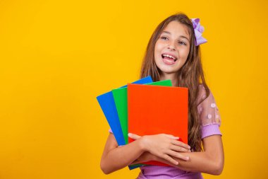 Okula giderken elinde kitaplarla gülümseyen güzel bir kız. yakın plan, izole edilmiş sarı arka plan, çocukluk. Çocuk kucaklama defterleri. Yaşam tarzı, ilgi, hobi, boş zaman, boş zaman